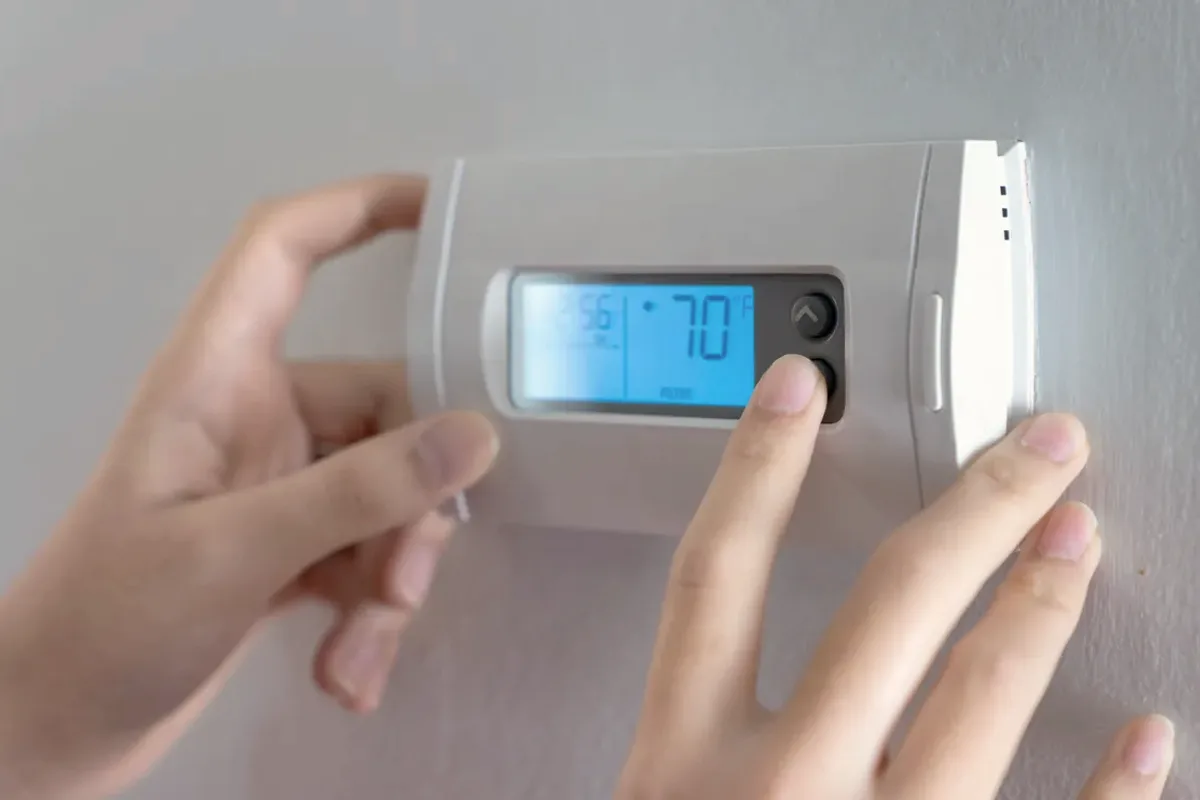 Hands adjusting a digital wall thermostat