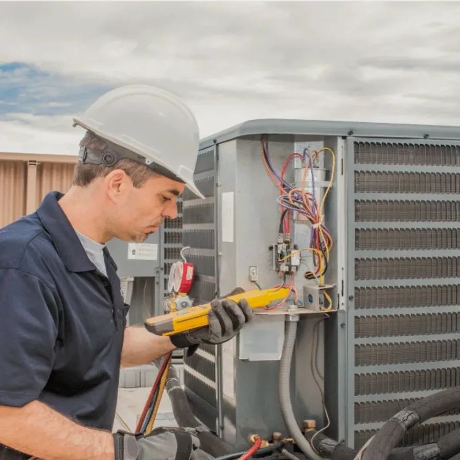 HVAC technician in a hard hat testing an outdoor air conditioner with a multimeter